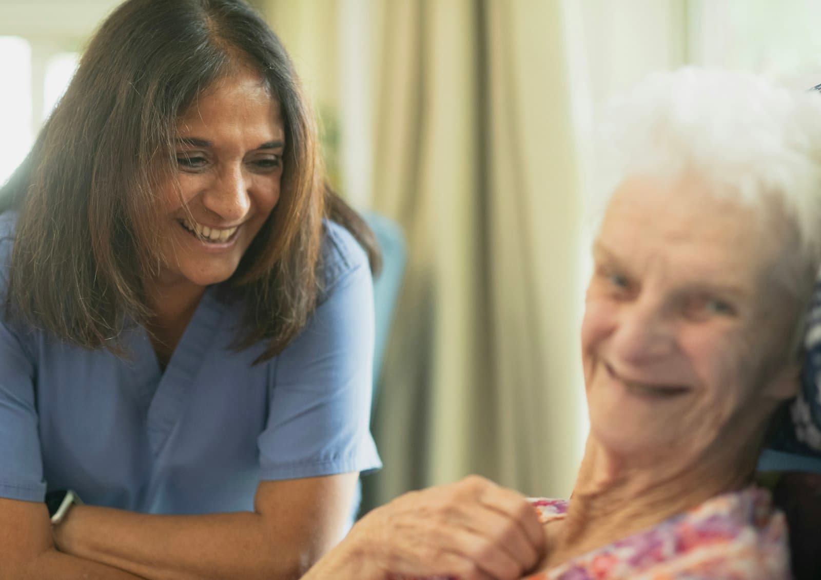 A home-care nurse laughing with an elderly patient in her living room